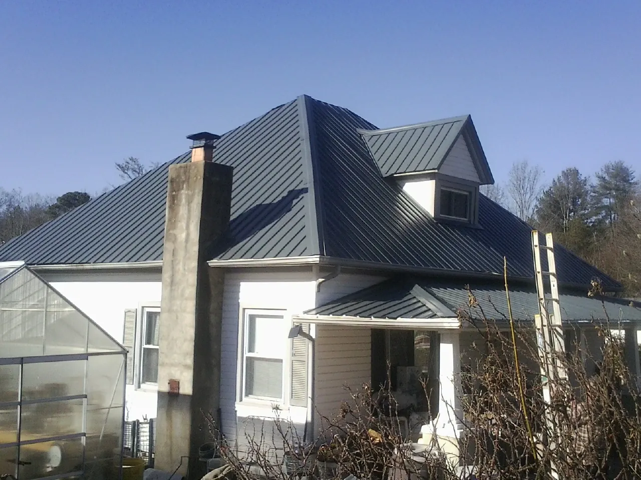 Dark blue standing seam metal roof on a white farmhouse with dormer — Slate & Tile Roof Repair by Roofing Brothers in Sturtevant