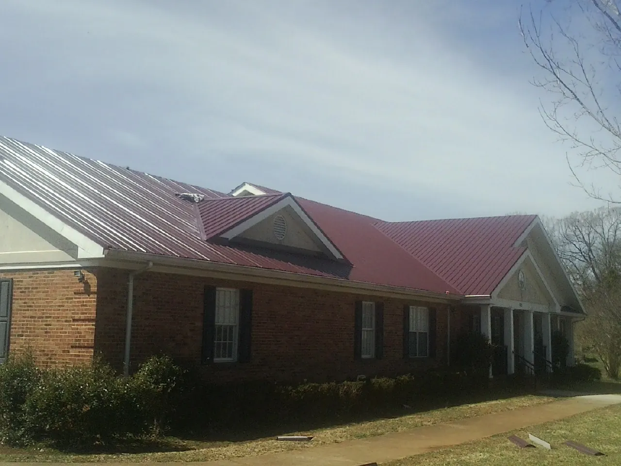 Red metal roof with gabled entries on a long brick building, from a Hail Damage Roof Repair job in Sturtevant