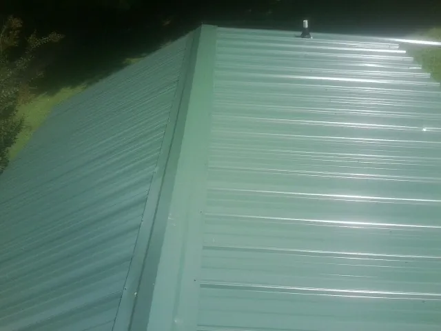 New green metal panels meeting at the ridge of a roof — Flat Roof Repair work by our crew in Sturtevant