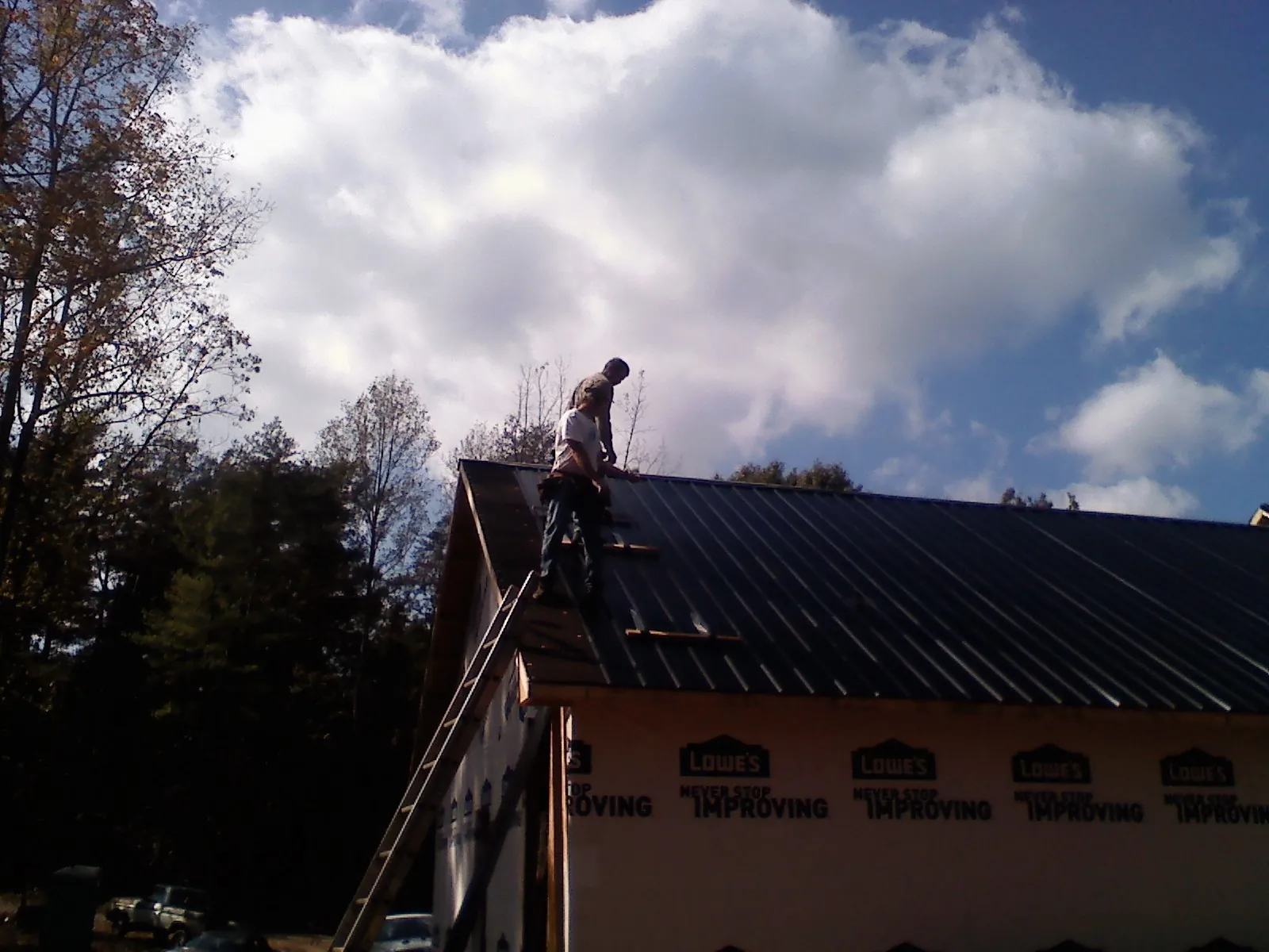 Roofer fastening dark metal panels high against a cloudy sky, from a Roof Inspection job in Sturtevant