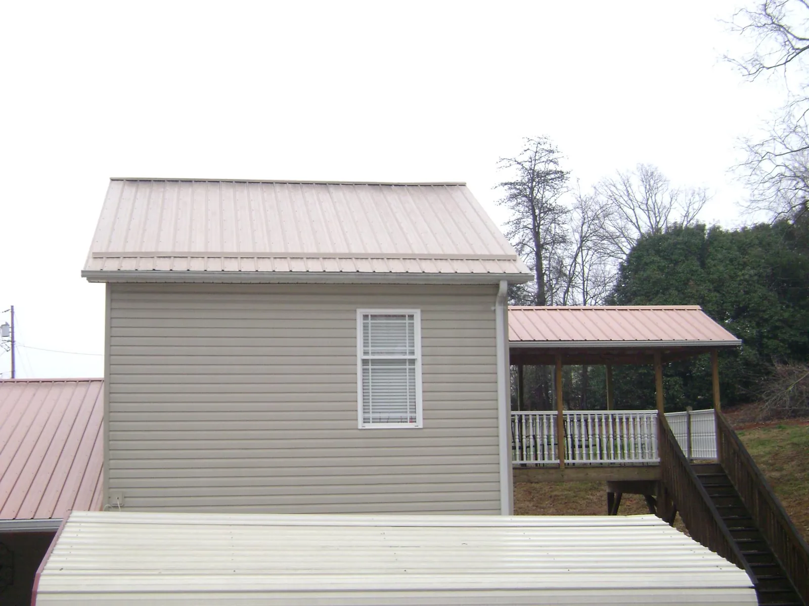 Tan metal roofs on a two story addition and attached porch, from a Roof Replacement job in Sturtevant
